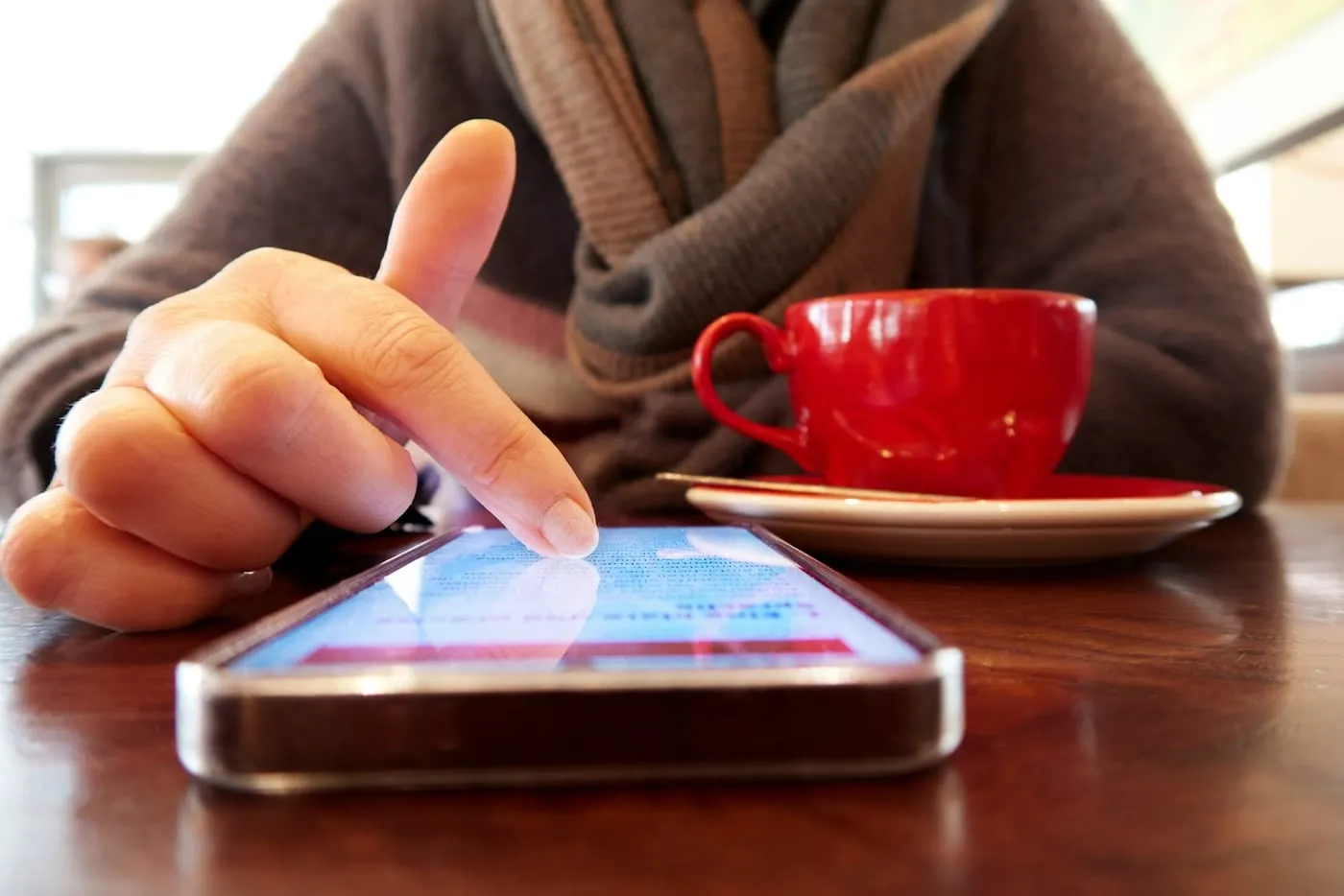 A person browsing on a phone beside a cup of coffee